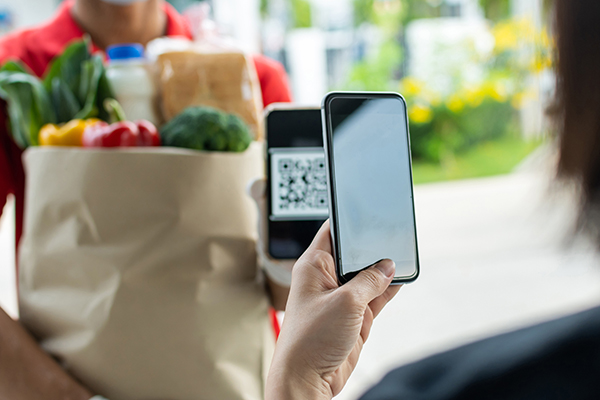 customer hand using digital mobile phone scan QR code paying for buying fresh food set bag from food delivery service man, express delivery, digital payment technology and fast food delivery concept