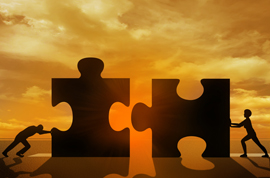 Silhouette image of two business people assembling two big puzzle pieces in front of sunset.